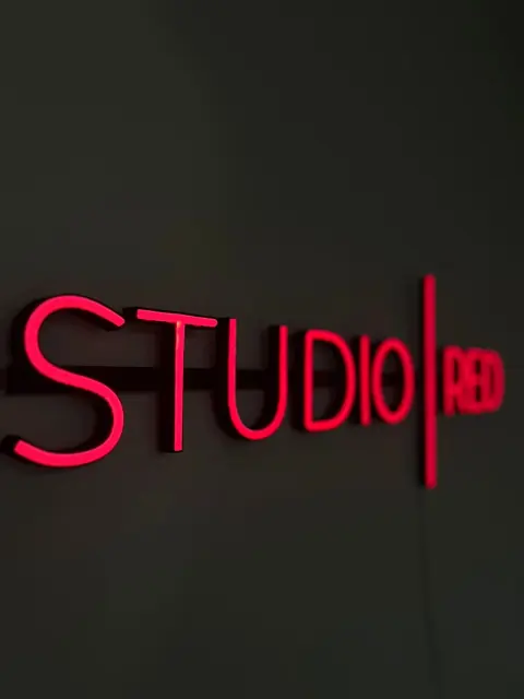 Raudonas LED neoninis studijos logotipas ant tamsios sienos